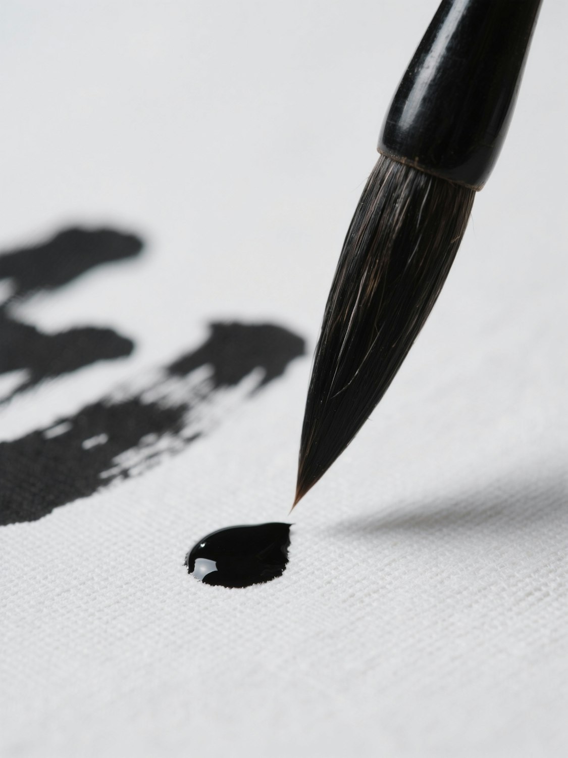 A brush drawing a stroke of black ink across a white canvas, the bristles bending under pressure.